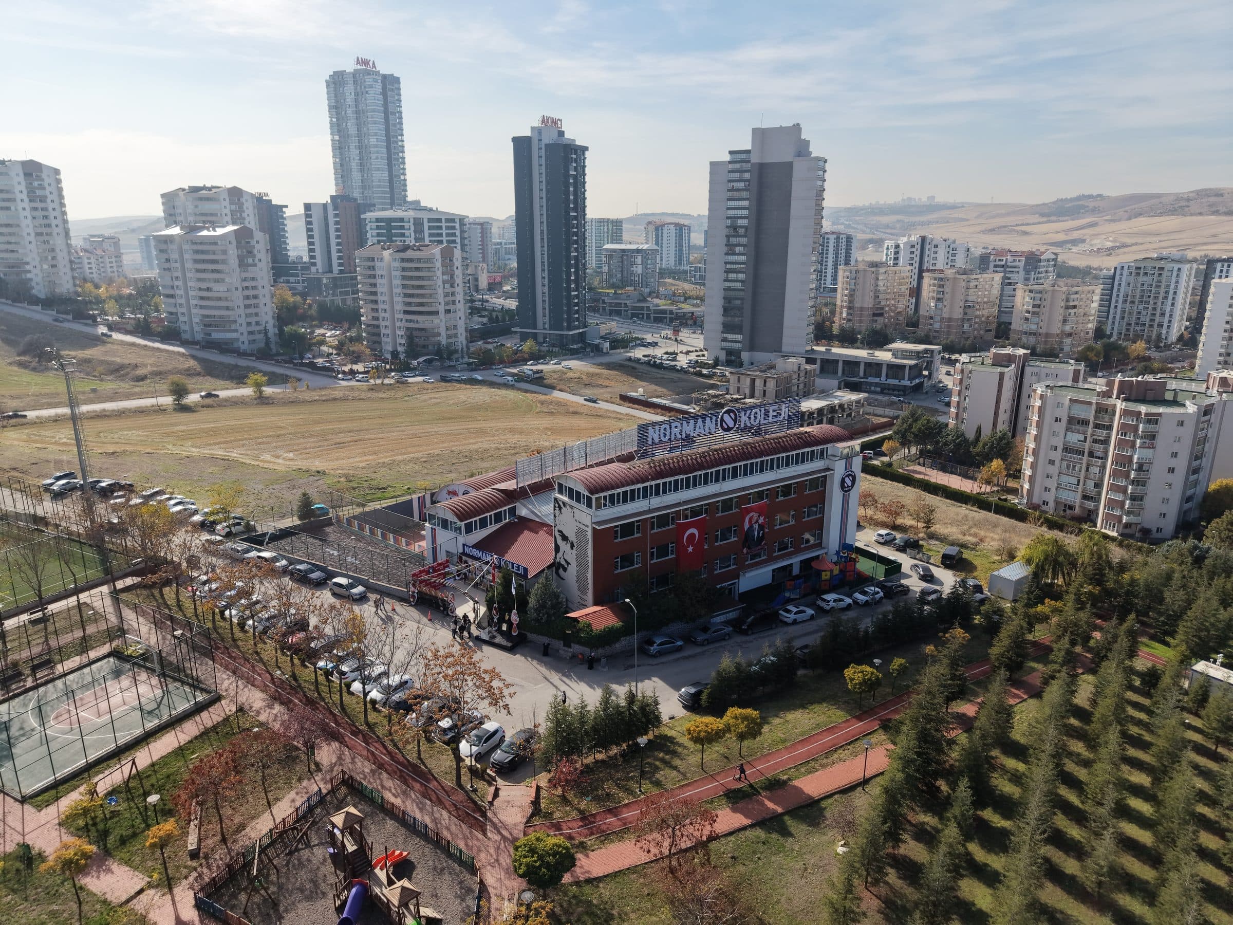 Norman Koleji binasının havadan görünümü: kırmızı çatılı dört katlı okul, çatıda NORMAN KOLEJİ tabelası, arkada Yaşamkent'in konutları.