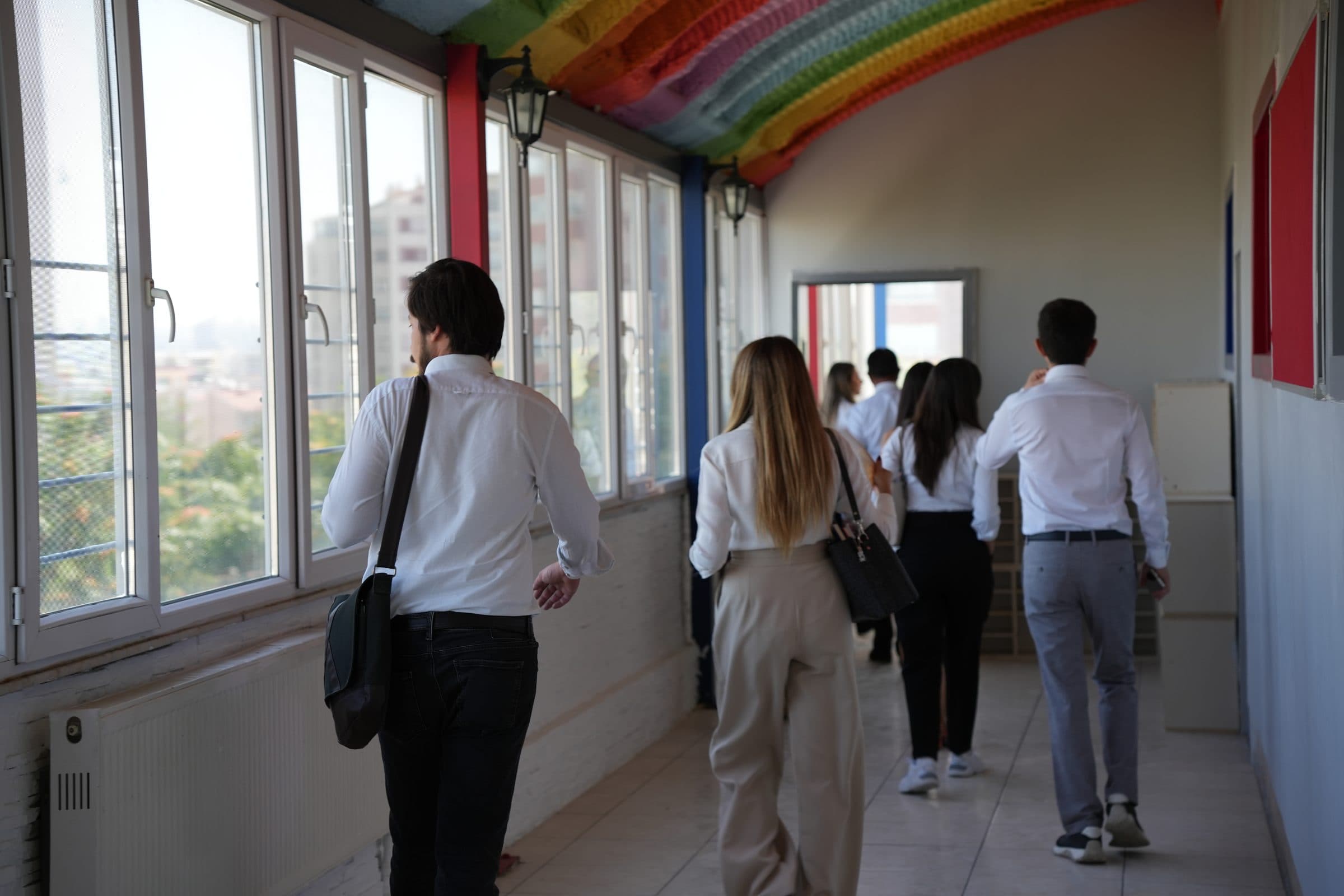 Pencereleri dışarıya bakan aydınlık koridor, renkli tavanın altında yürüyen öğretmenler.