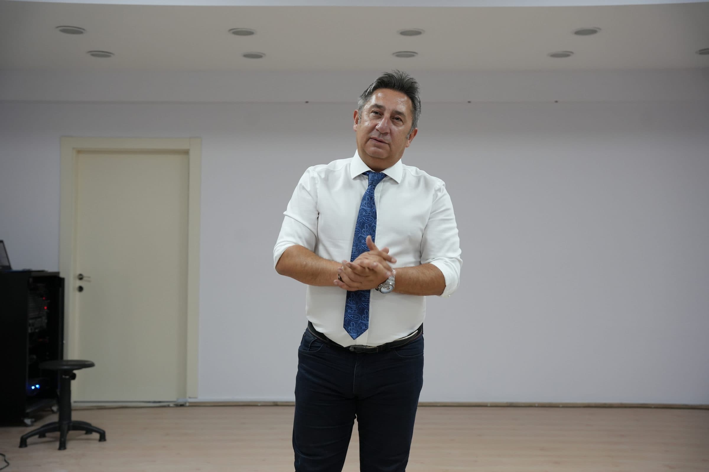 Öztuna Norman, salonda ellerini birleştirmiş, öğretmenlere konuşuyor.